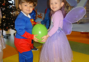 Dwoje uśmiechniętych dzieci tańczy w parze, w rączkach trzymają balon.